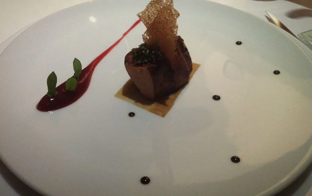 Pieczone foie gras z chrupkim listkiem, pasem buraczanego sosu i kropkami redukcji na białym talerzu